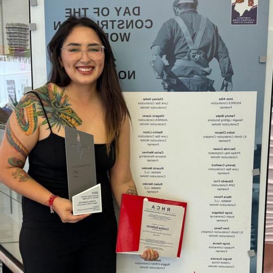 A woman holds an award 和 certificate in front of a photo backdrop.